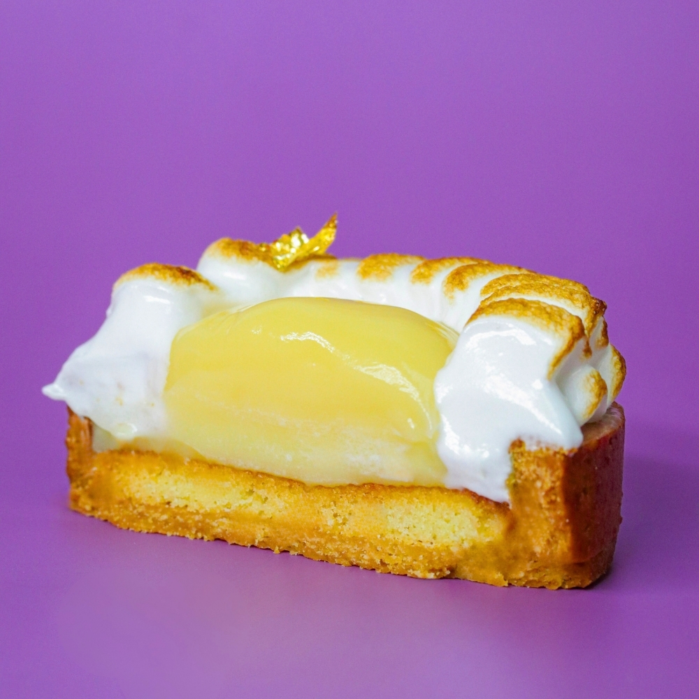 Yuzu curd tart slice with toasted meringue on a purple background