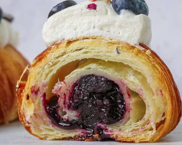 Laminated pastry with blueberry filling and cream topping, shown cross-section with flaky layers